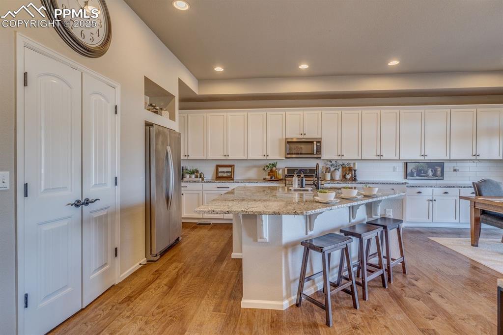 Image 21 of 50: Kitchen with white cabinets, a breakfast bar, light stone countertops, appl