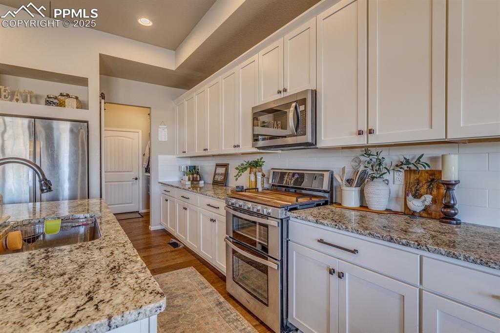 Image 23 of 50: Kitchen with appliances with stainless steel finishes, white cabinetry, lig