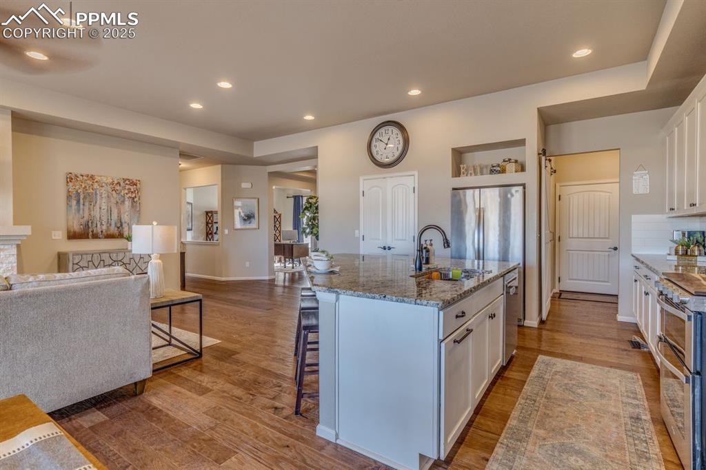 Image 24 of 50: Kitchen with open floor plan, white cabinetry, light stone countertops, sta