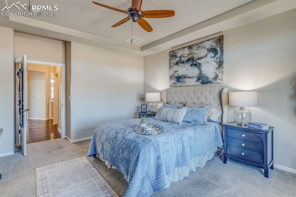Image 28 of 50: Carpeted bedroom featuring a raised ceiling and a ceiling fan