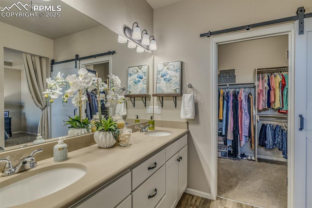 Image 30 of 50: Full bathroom with double vanity, a walk in closet, and light wood-style fl