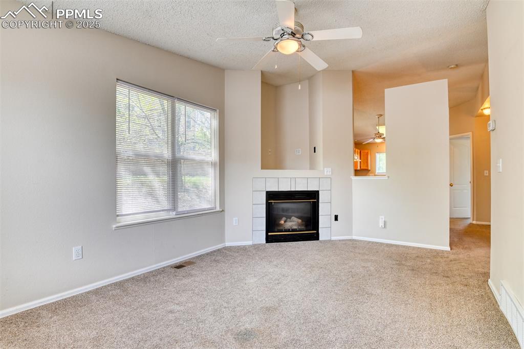 Image 3 of 36: Unfurnished living room with ceiling fan, carpet floors, a tiled fireplace,