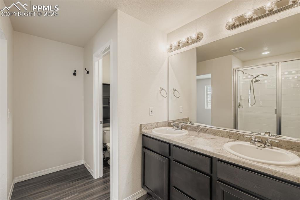 Image 10 of 26: Bathroom with double vanity, a shower stall, and dark wood-type flooring