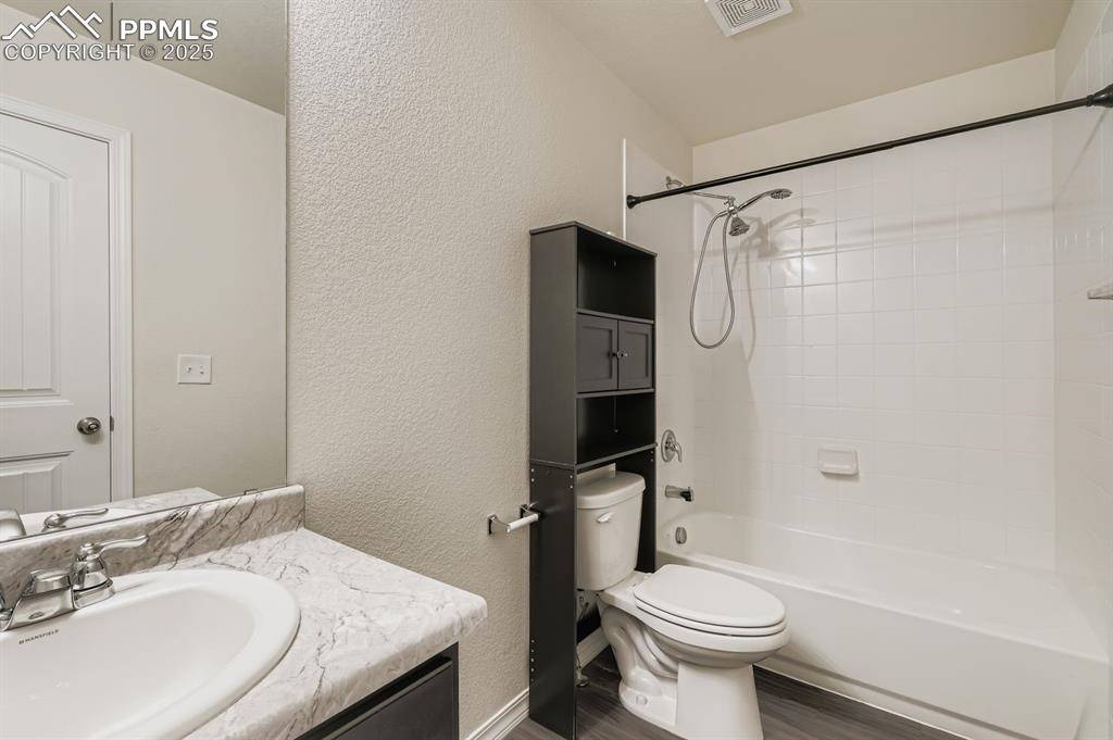 Image 17 of 26: Full bath with a textured wall, vanity, shower / bath combination, and wood
