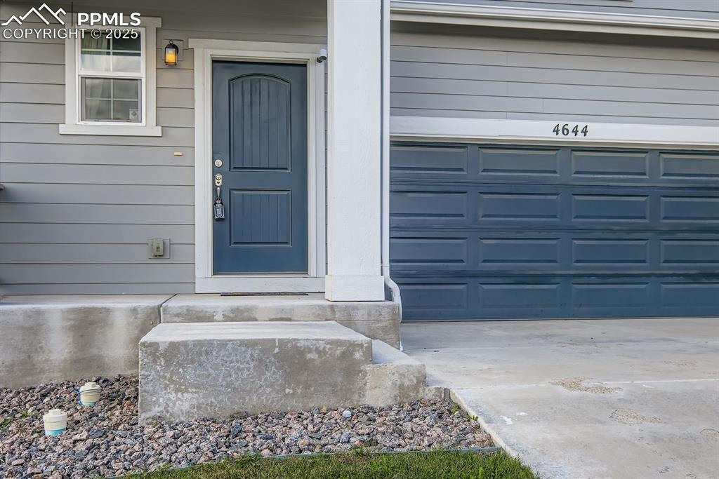 Image 22 of 26: Doorway to property featuring a garage and concrete driveway