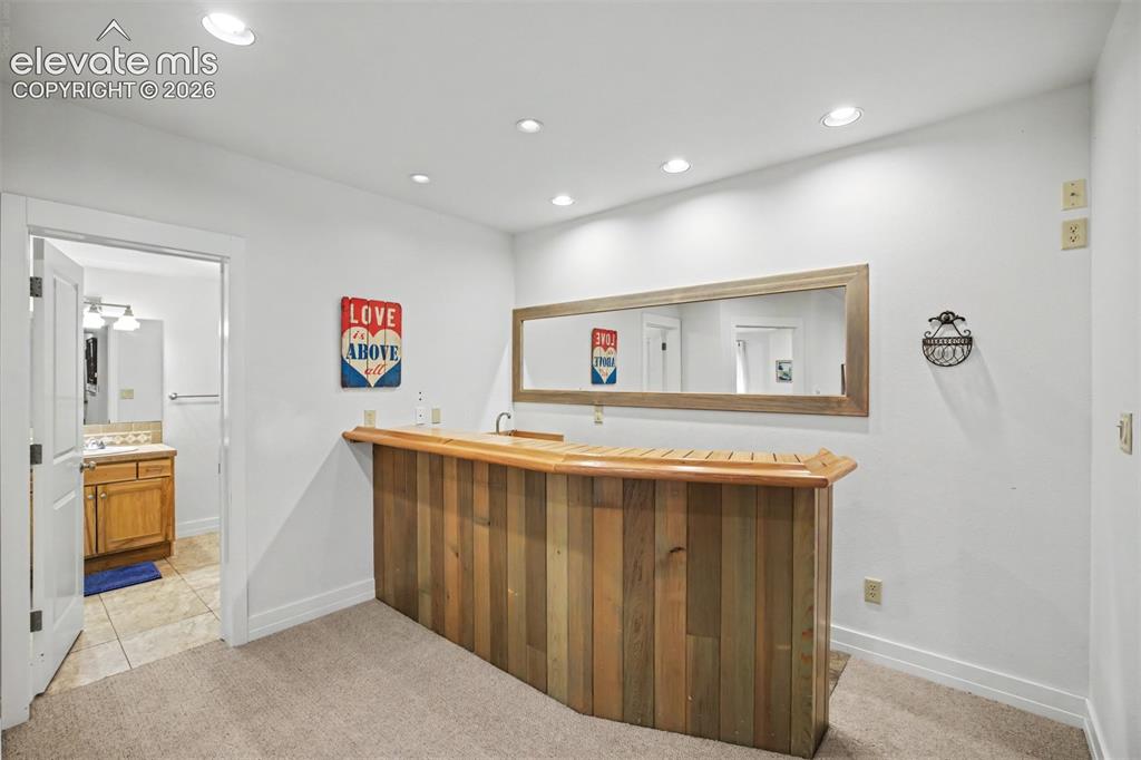 Image 37 of 50: The basement wet bar features a sink, mini refrigerator and built-in cabine