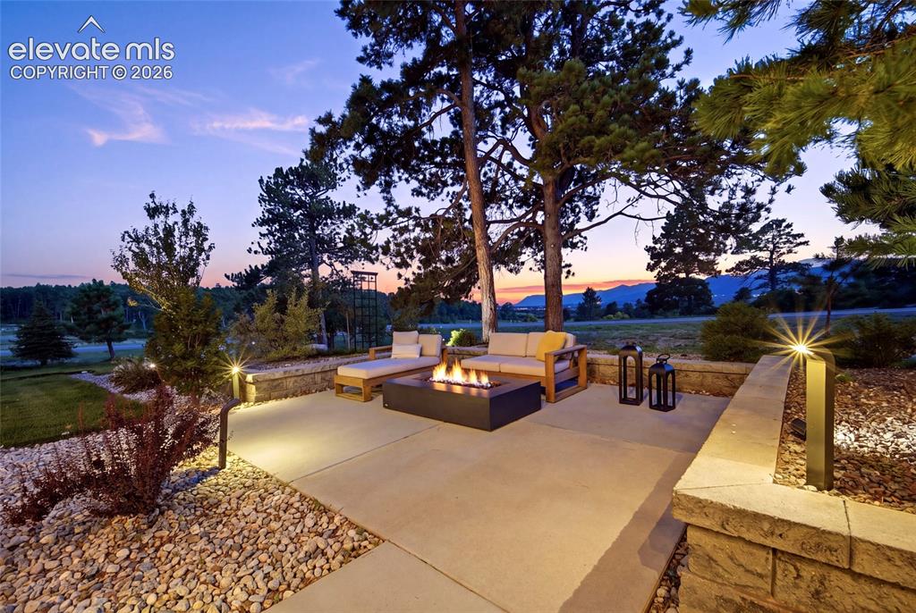 Image 10 of 50: Expansive patio with a built-in fire feature, surrounded by landscaping wit