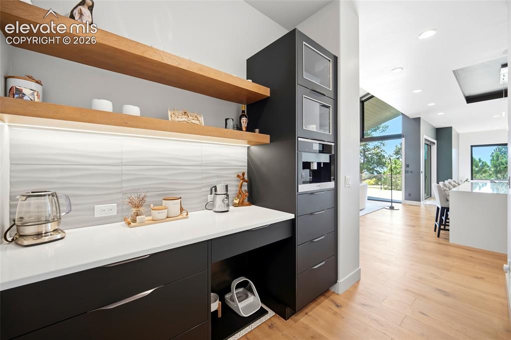 Image 21 of 50: Built-in coffee station with stacked appliances, open wood-finish shelving,