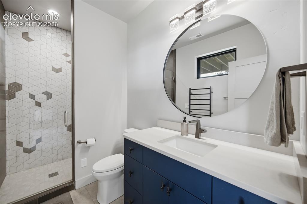 Image 46 of 50: Walk-in shower with geometric tile, dark blue vanity cabinetry, white count