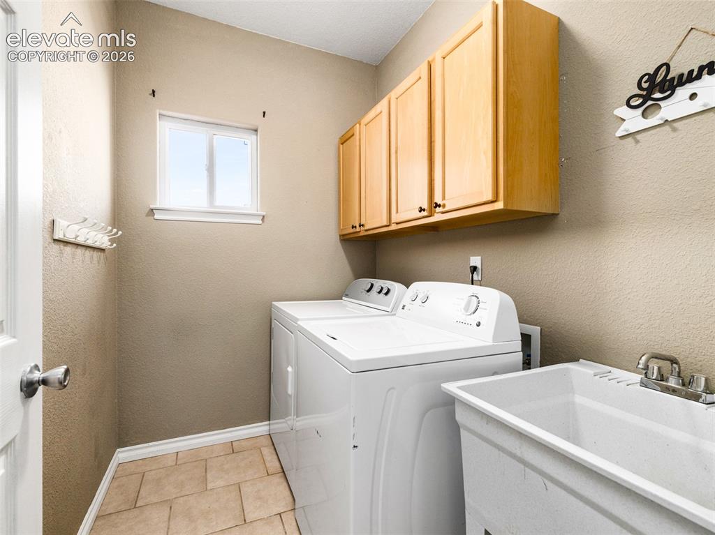 Image 11 of 49: Laundry room featuring light wood cabinetry, a utility sink, and tile floor