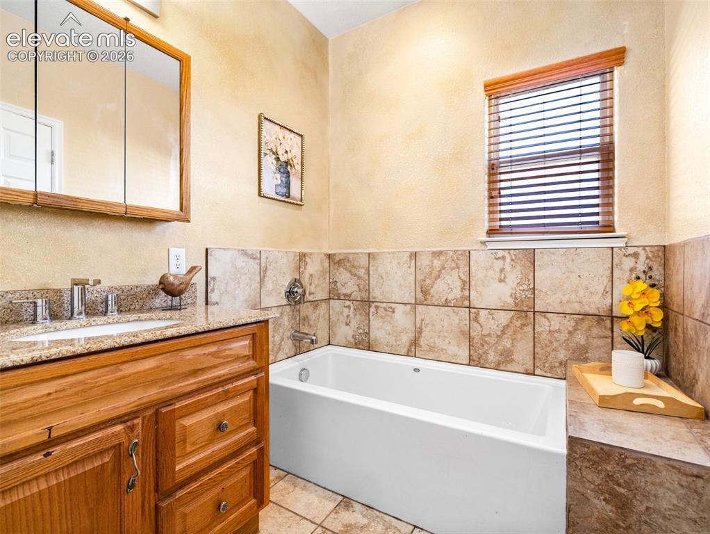 Image 14 of 49: Integrated bathtub with tiled surround, wood-finish vanity with a granite c