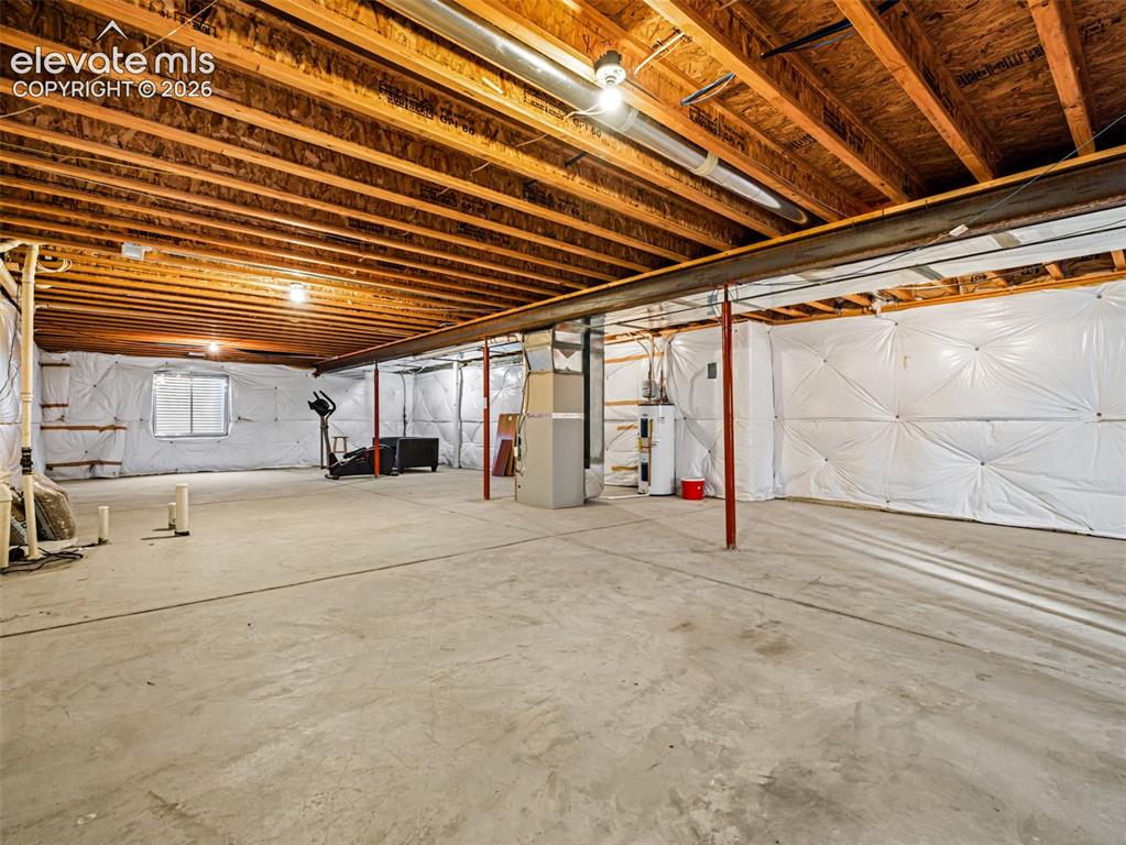 Image 20 of 49: Unfinished lower level with concrete flooring, exposed wood joists, utility