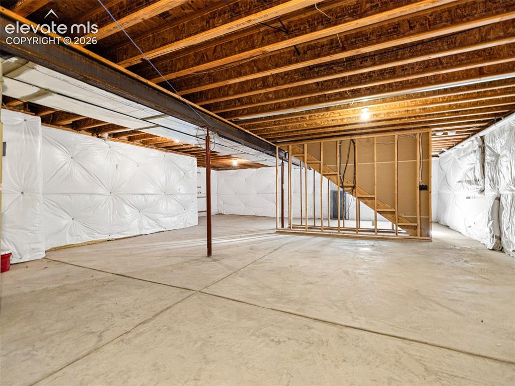 Image 21 of 49: Unfinished basement with concrete flooring, visible wood ceiling joists, an