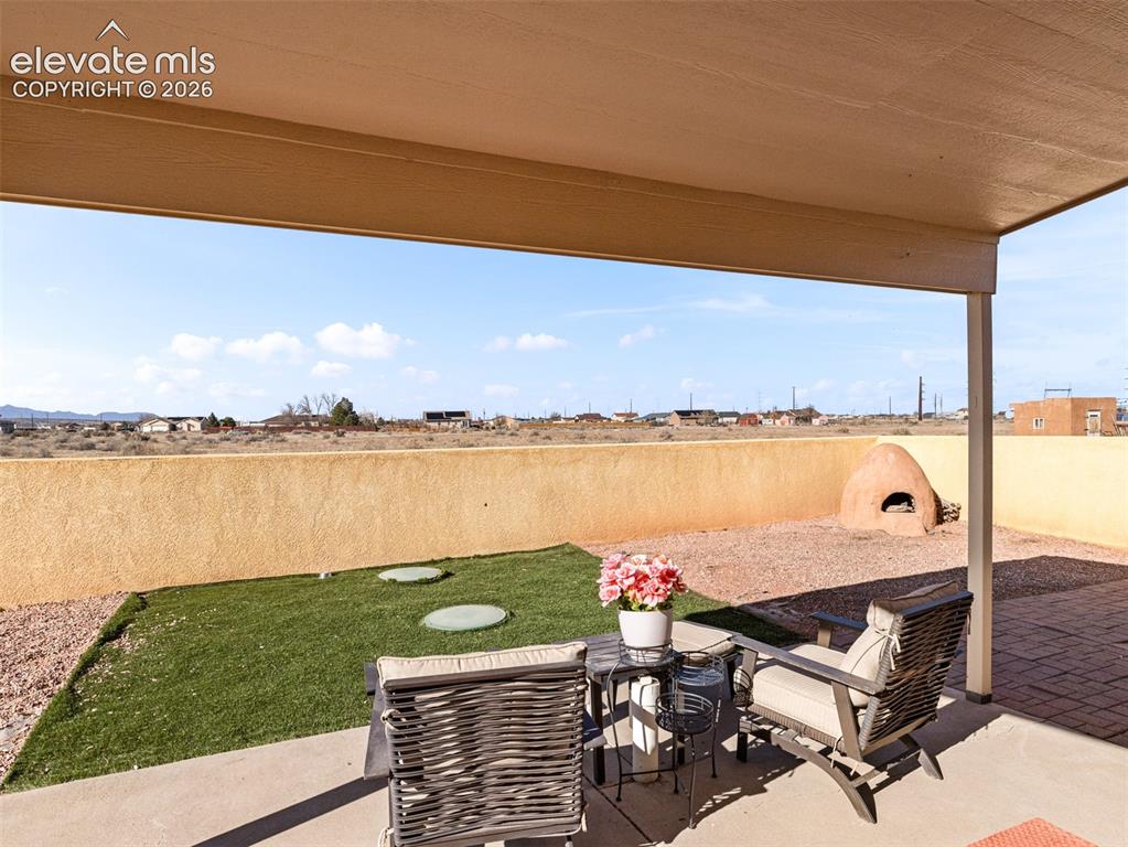 Image 22 of 49: Covered patio with concrete flooring, stucco wall, artificial turf area, an