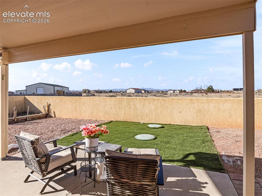 Image 23 of 49: Covered patio with concrete flooring, low perimeter wall, and a grass area