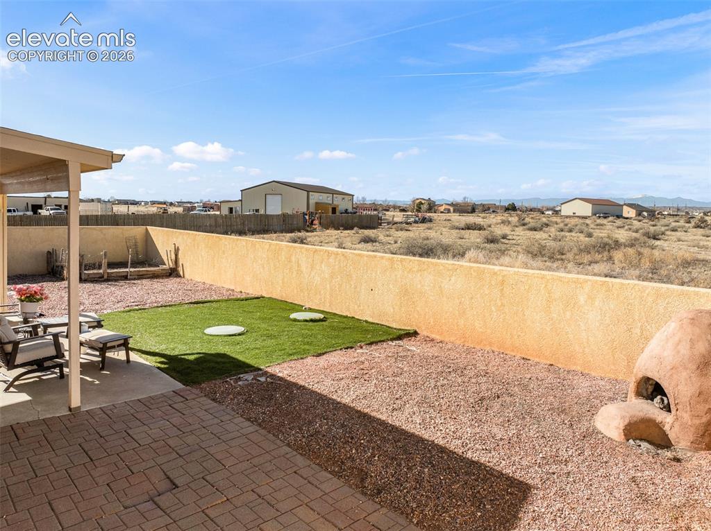 Image 33 of 49: Covered patio with paver flooring, low-maintenance landscaping with gravel 
