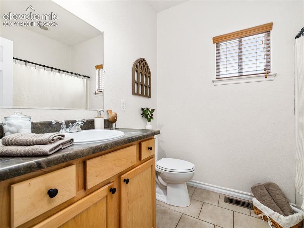 Image 38 of 49: Vanity with natural wood cabinetry and dark countertop, integrated sink wit
