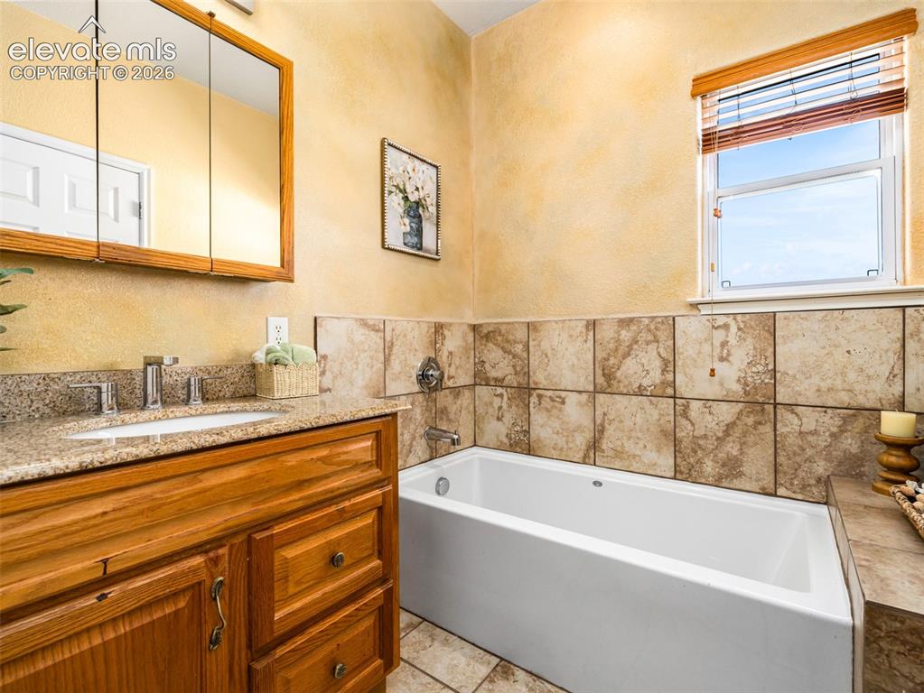 Image 46 of 49: Built-in bathtub with tiled surround, wood-finish vanity with granite count