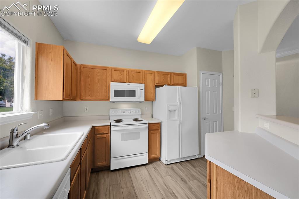 Image 8 of 18: Kitchen with white appliances, light wood-type flooring, light countertops,