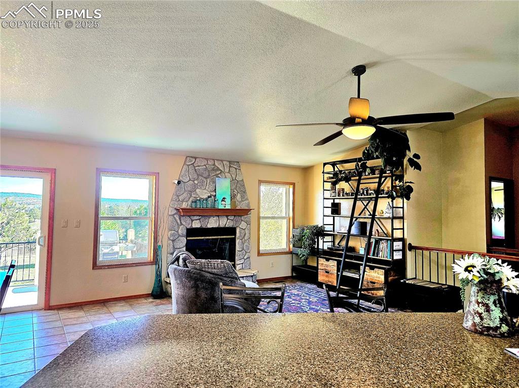 Image 7 of 44: Tiled living area featuring a textured ceiling, a fireplace, and ceiling fa