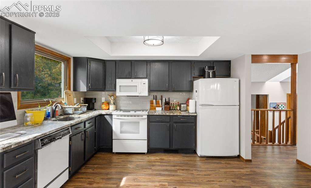 Image 10 of 21: Kitchen featuring white appliances, a raised ceiling, dark wood-type floori