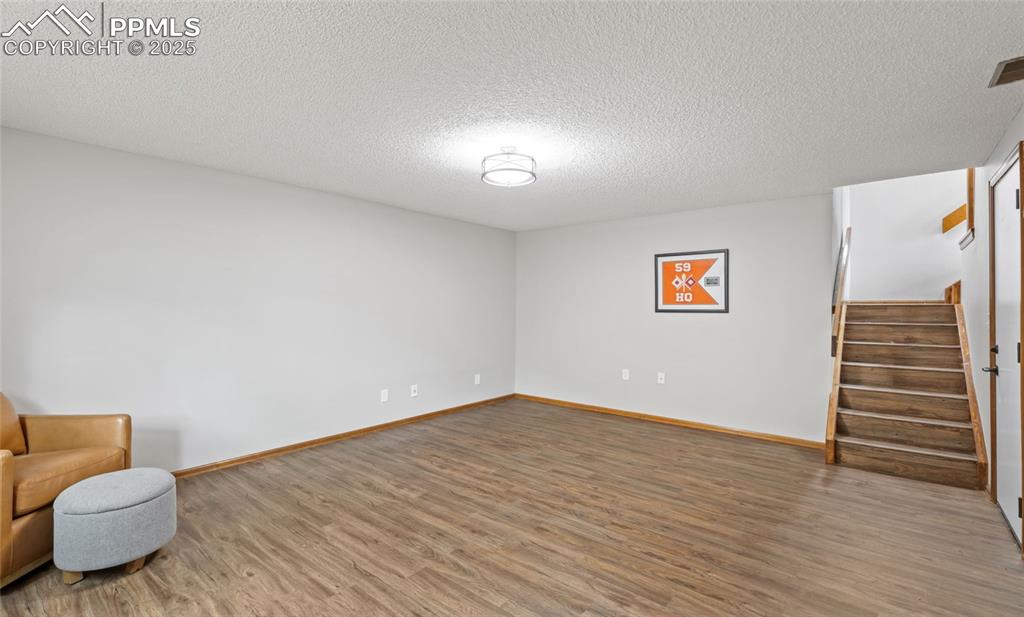 Image 18 of 21: Unfurnished room featuring stairs, wood finished floors, and a textured cei