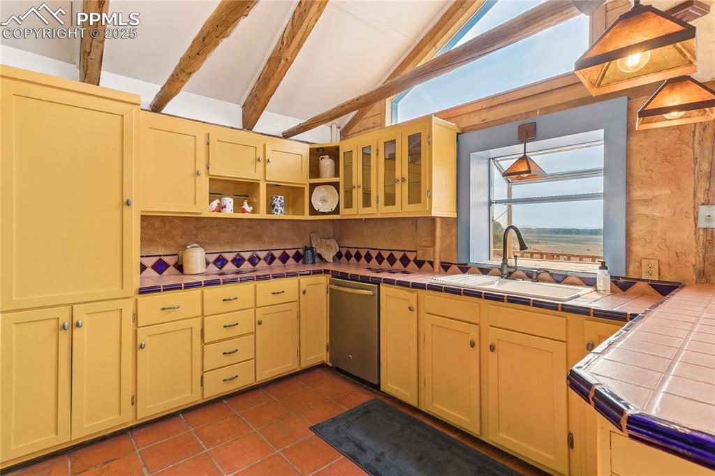 Image 14 of 50: Kitchen with tile counters, hanging light fixtures, open shelves, stainless
