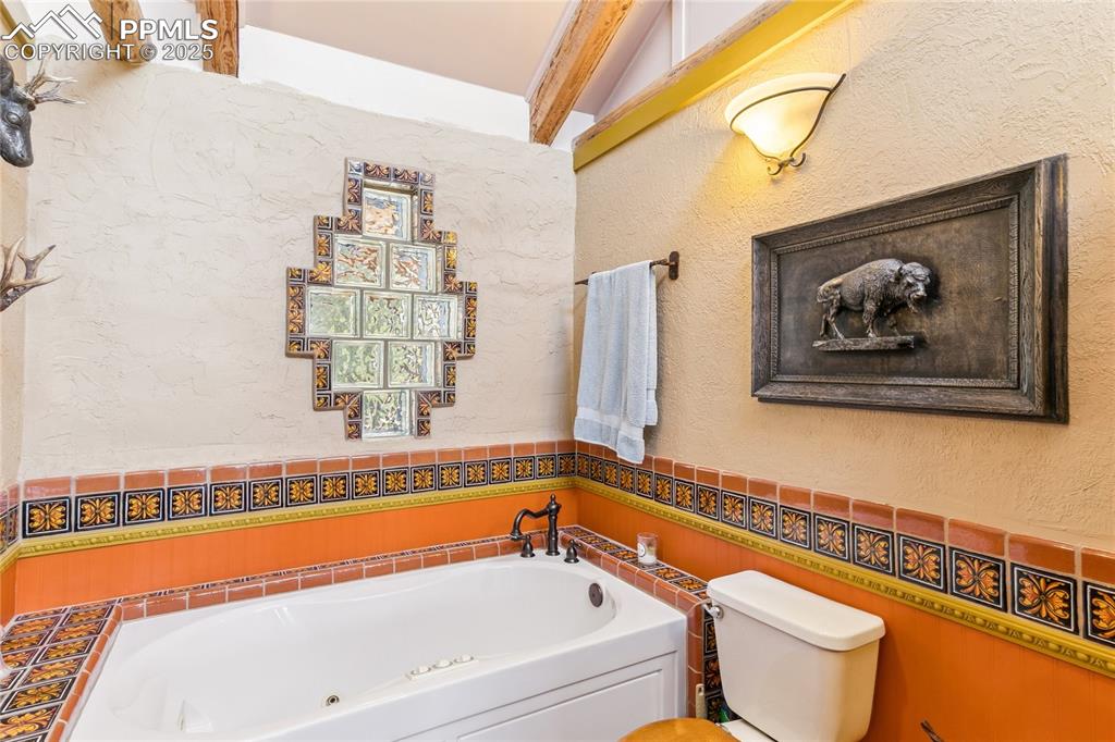 Image 18 of 50: 3/4 Bathroom featuring a tub with jets, a textured wall, and wainscoting