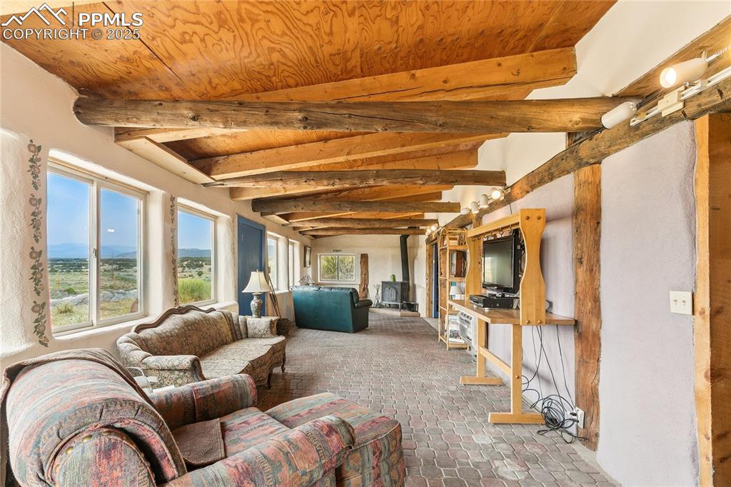 Image 21 of 50: Living area with a wood stove and a wood ceiling with exposed beams
