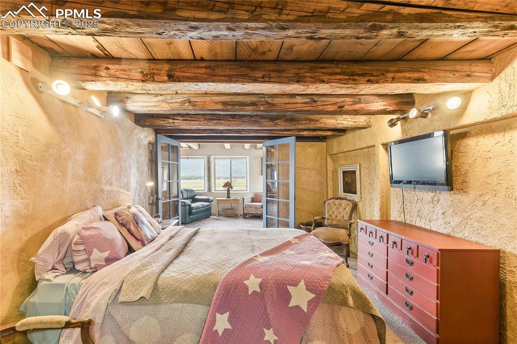 Image 39 of 50: Bedroom with a wooden ceiling with exposed beams and a textured wall