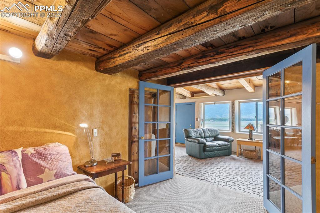 Image 40 of 50: Bedroom with a wood ceiling with exposed beams, french doors, and carpet fl