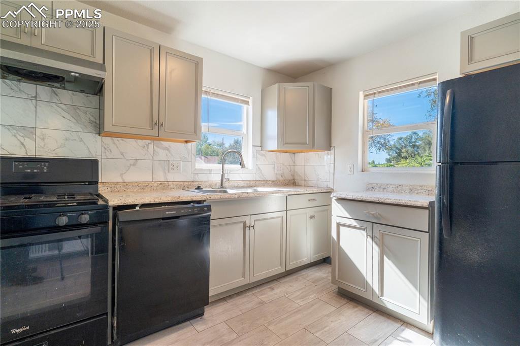 Image 5 of 11: Kitchen with black appliances, tasteful backsplash, under cabinet range hoo