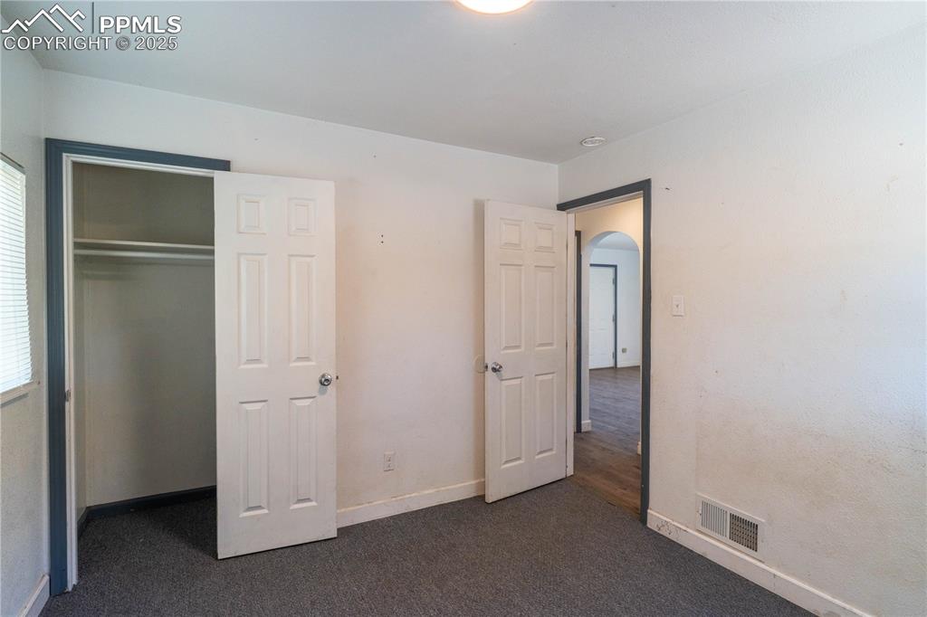Image 6 of 11: Unfurnished bedroom with arched walkways, dark colored carpet, and a closet
