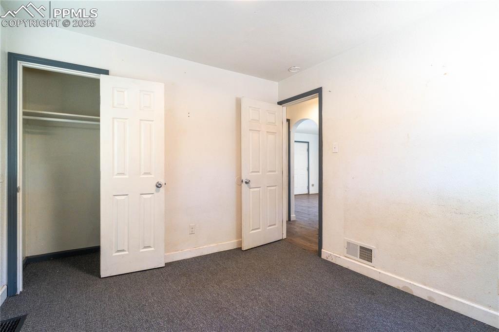 Image 8 of 11: Unfurnished bedroom with arched walkways, dark colored carpet, and a closet