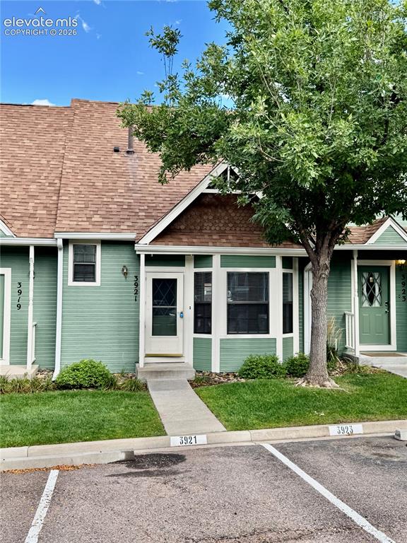Caption: Green siding exterior with a brown shingle roof, complemented by a mature tree and manicured lawn