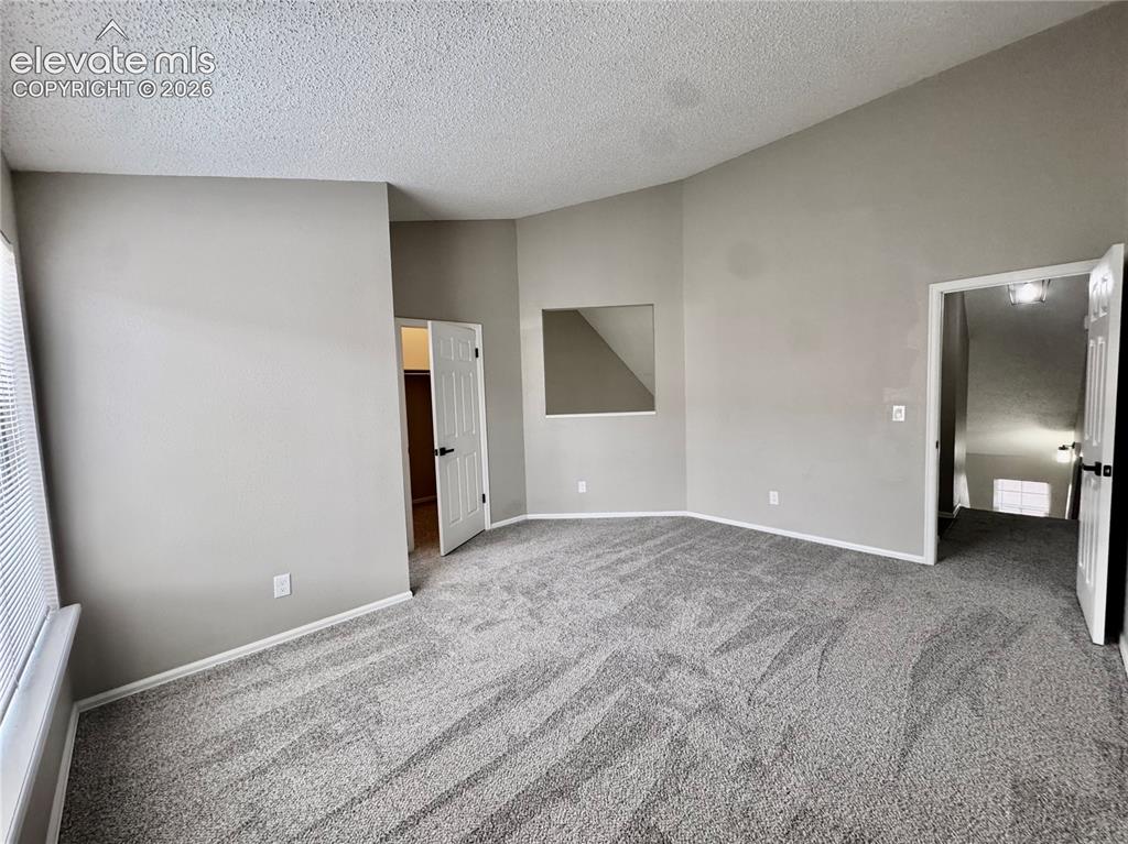 Image 14 of 20: Vaulted ceiling, neutral wall paint, gray carpeting, white trim, and a wind
