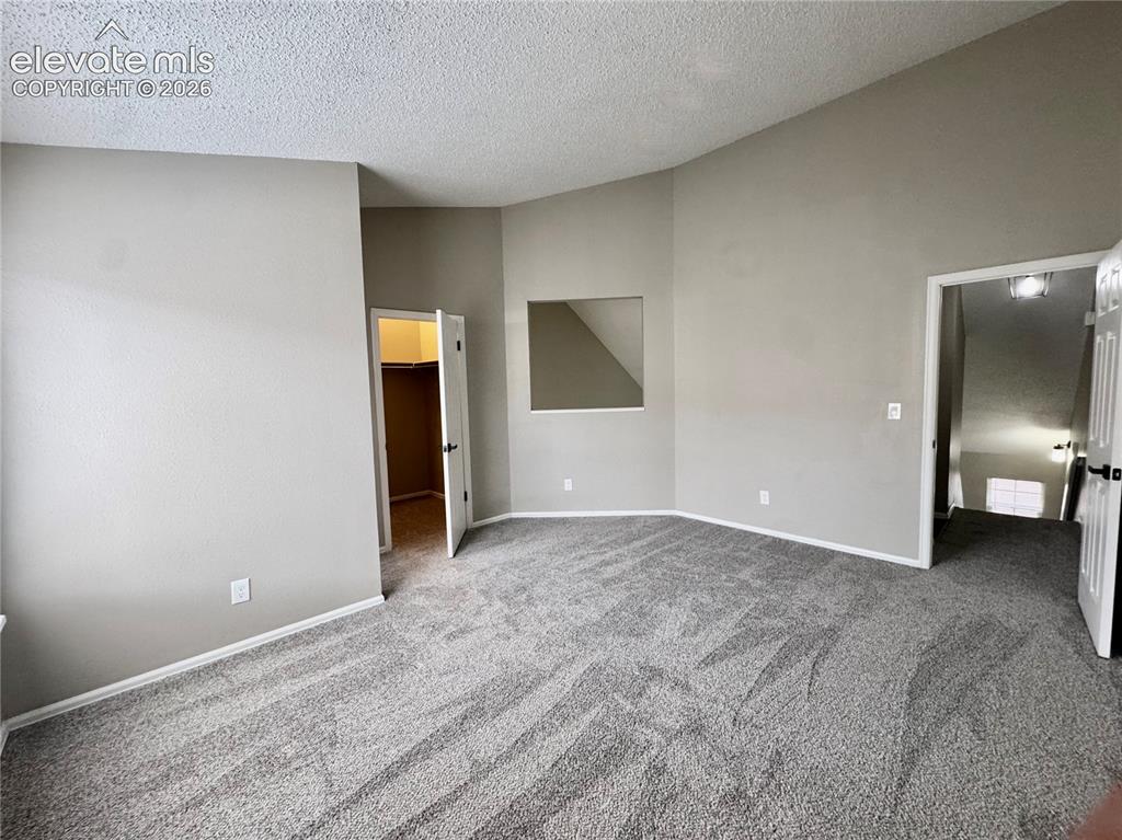 Image 15 of 20: Vaulted ceiling, neutral wall paint, gray carpeting, and a built-in wall ni