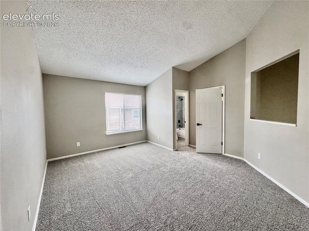 Image 16 of 20: Vaulted ceiling with textured finish, neutral wall paint, gray carpeting, a