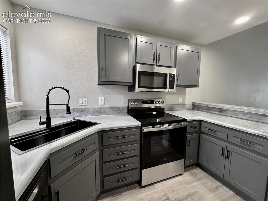 Image 5 of 20: Gray cabinetry, stainless steel appliances, black sink, black faucet, and l