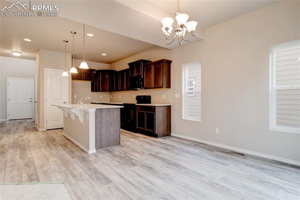 Image 10 of 24: Kitchen featuring a breakfast bar area, hanging light fixtures, black appli