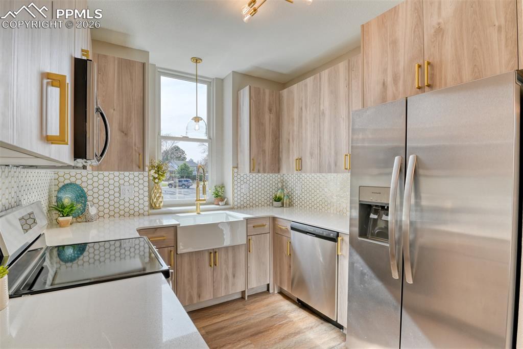 Image 15 of 44: Kitchen with stainless steel appliances, light stone counters, light wood f