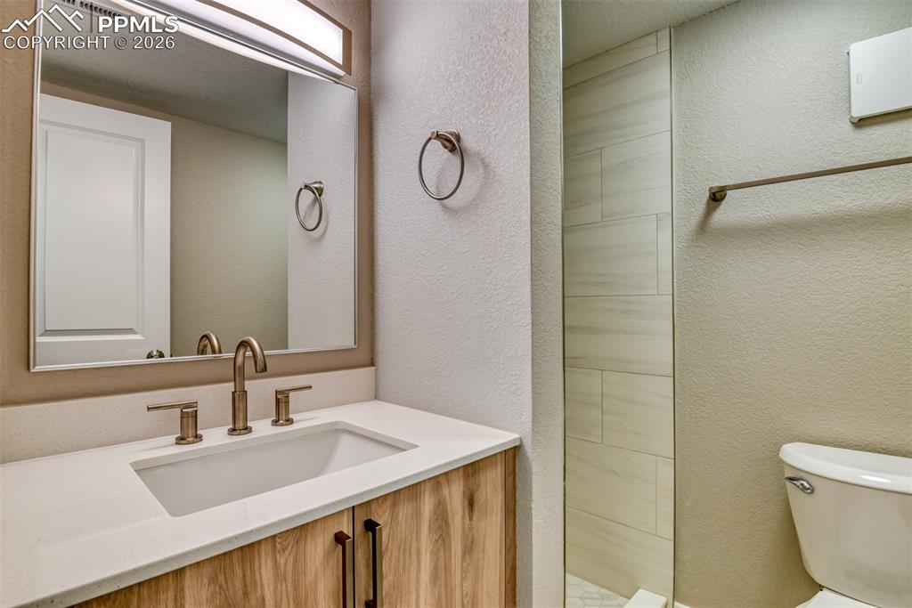 Image 39 of 44: Bathroom featuring a textured wall, vanity, and tiled shower