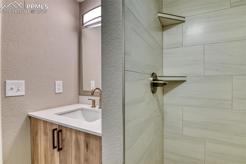 Image 40 of 44: Bathroom with a textured wall, vanity, and a tile shower