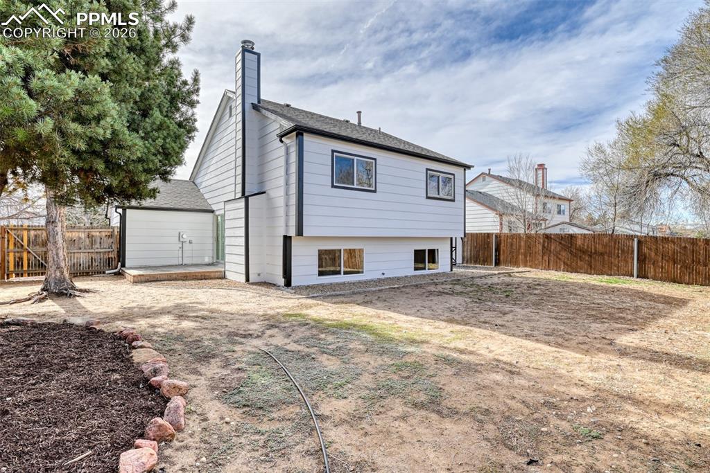 Image 43 of 44: Back of house featuring a fenced backyard, a chimney, and a shingled roof