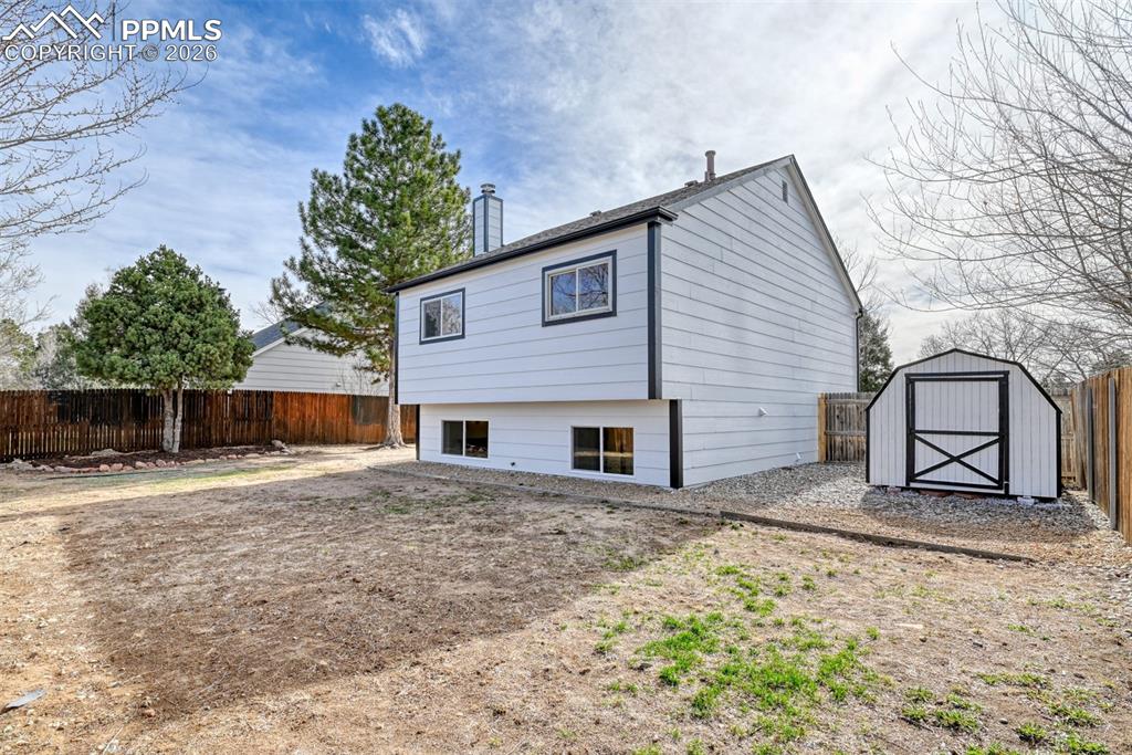 Image 44 of 44: Back of house with a fenced backyard, a storage shed, and a chimney