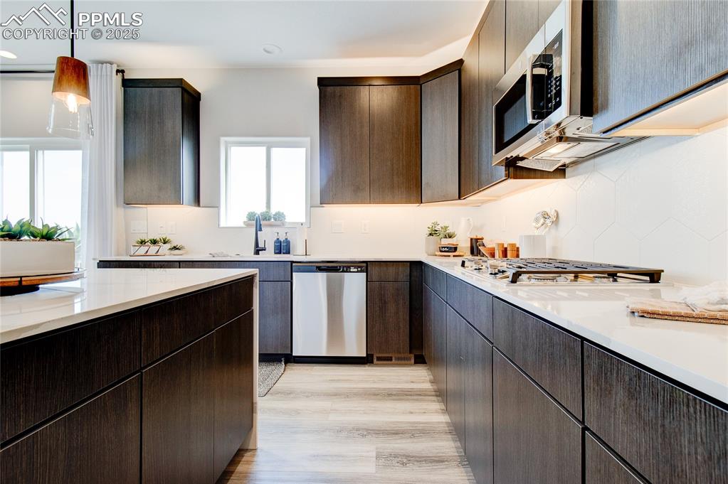 Image 18 of 32: Kitchen with stainless steel appliances, decorative backsplash, light wood 
