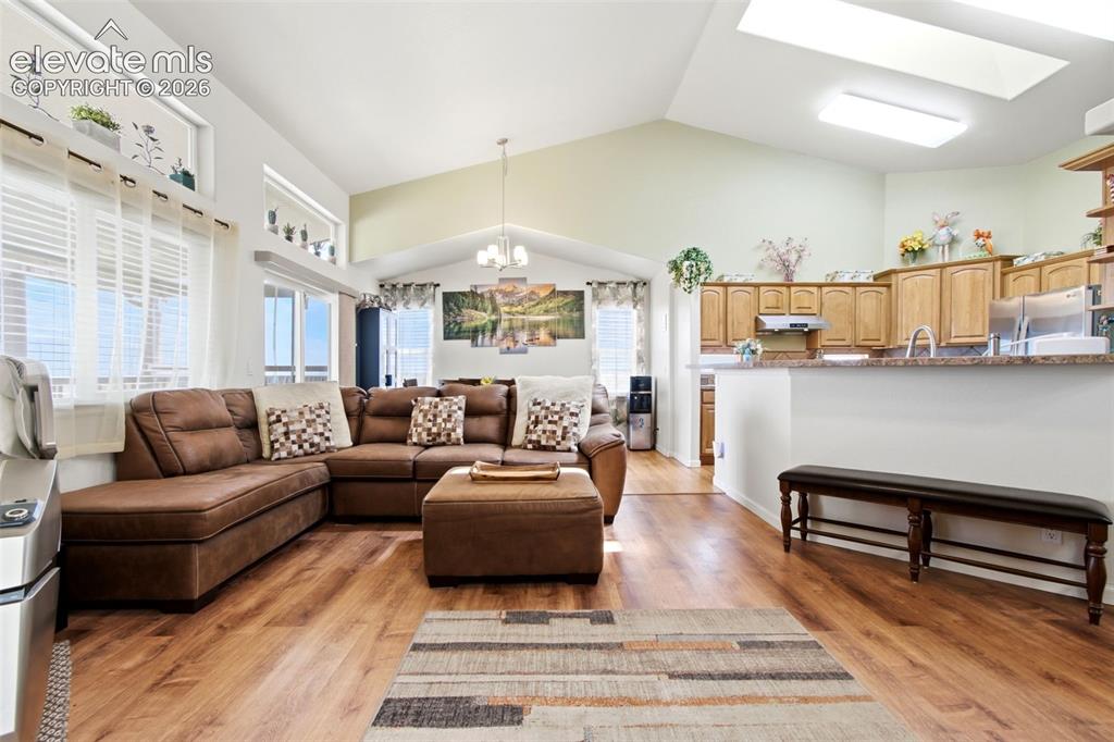 Image 10 of 44: Open-concept living area featuring warm laminate wood-finish flooring, vaul