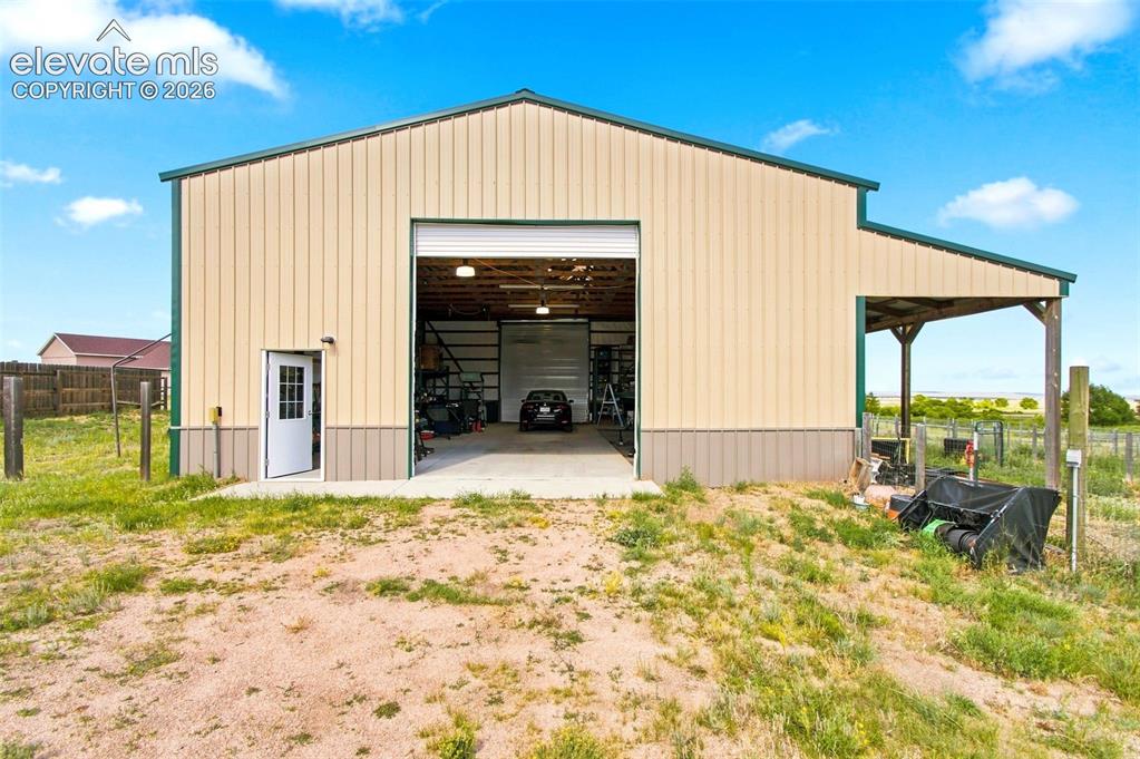 Image 33 of 44: Metal-sided outbuilding featuring a large roll-up door, a separate entry do