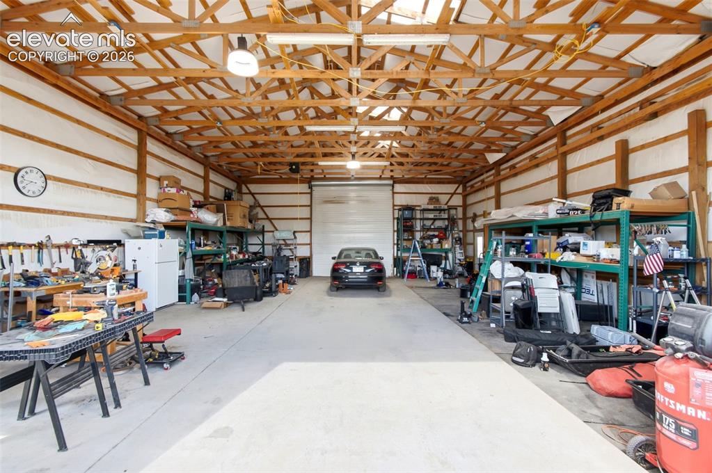 Image 35 of 44: Spacious barn/workshop with exposed wood beam ceiling, concrete flooring, a