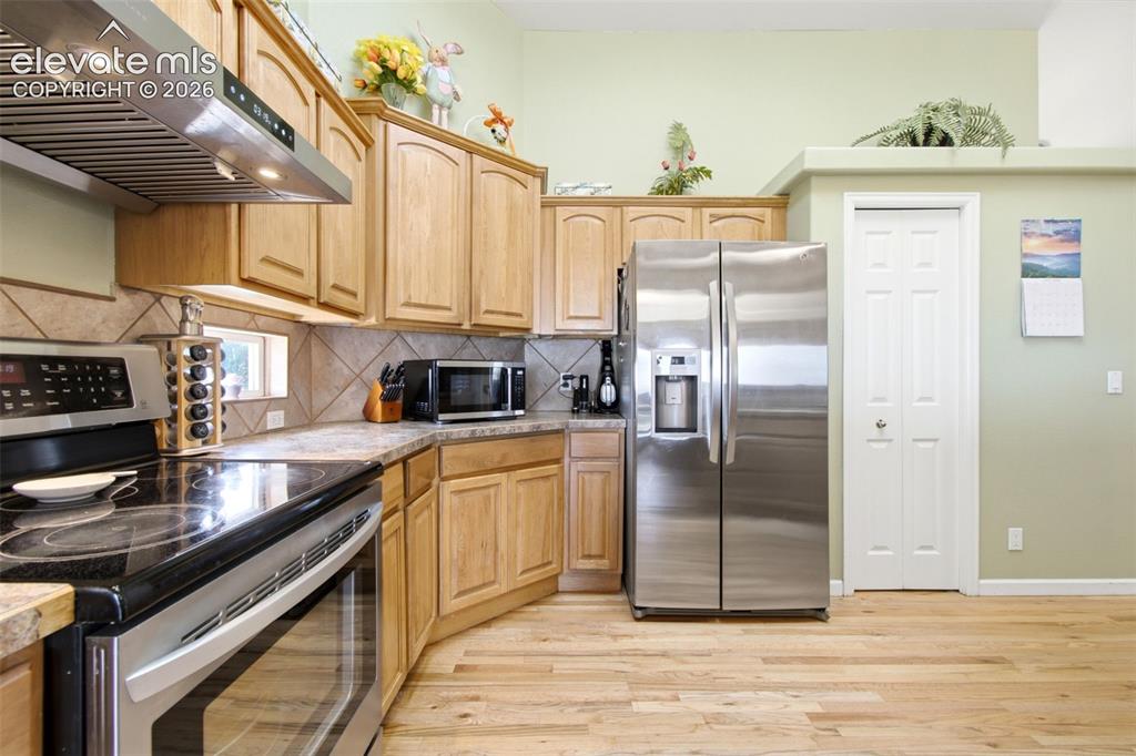 Image 5 of 44: Kitchen featuring light wood cabinetry, stainless steel appliances, tile ba